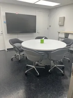 conference room with round table and five chairs, large mounted tv on the back wall