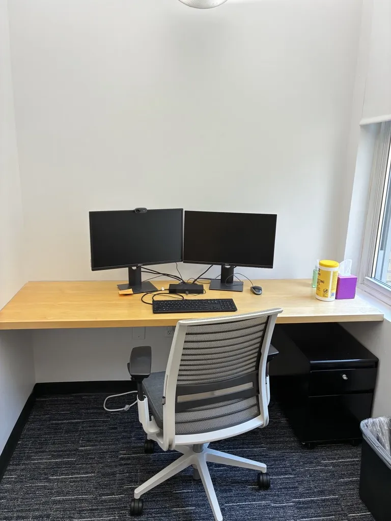 private office with desk, chair, 2 monitors against an empty wall, window to the right