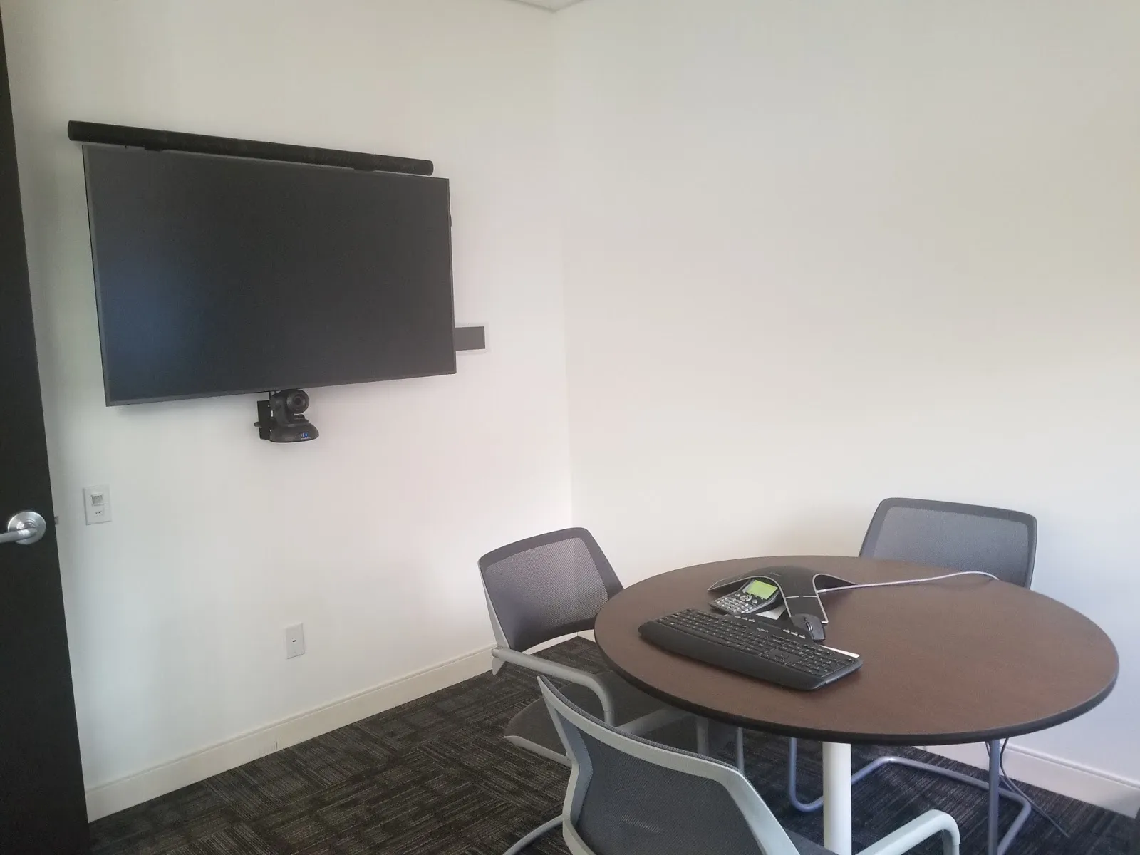 small conference room with round table and 3 chairs and wall mounted tv on the left