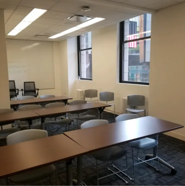 Large room with 3 rows of tables and chairs with two windows to the right of the room
