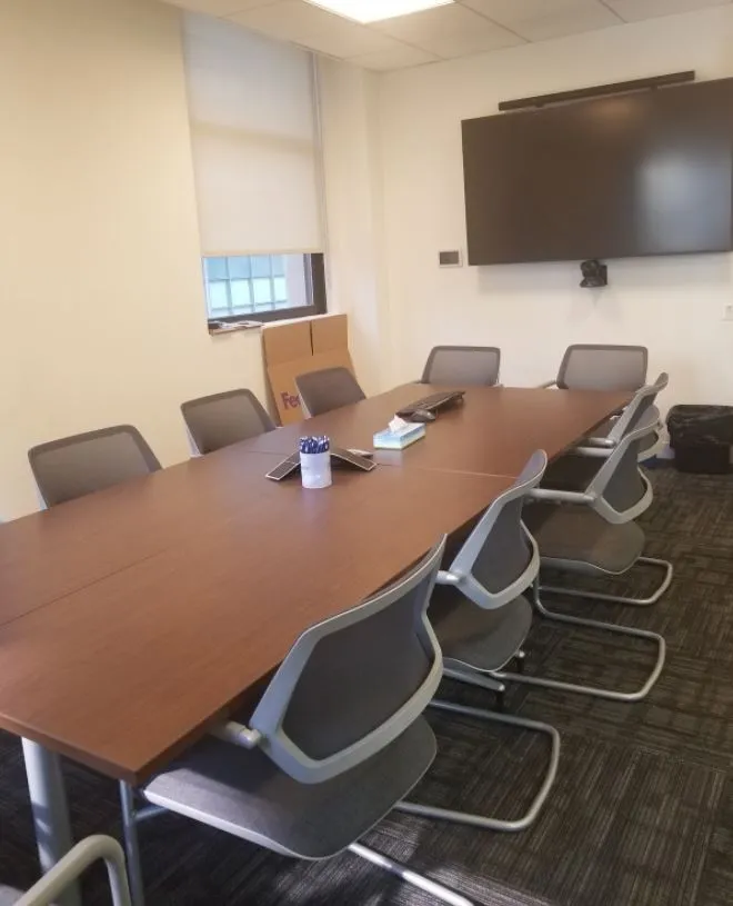 large conference table with 9 chairs surrounding 3 sides, with large wall mounted tv on far wall