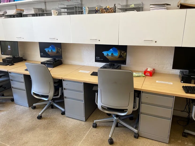 Long desk with 4 computer workstations, chairs and rolling cabinets under the table